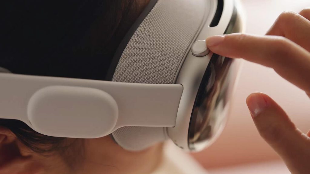 Extreme close up side on image of a person wearing Apple's Vision Pro headset. They are pressing a button on the top of the headset