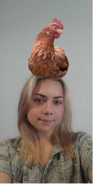 A selfie of a woman with an augmented reality chicken sitting on the top of her head