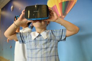 image of a young girl in a school dress holding a VR headset that she is wearing on her face