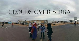 Screenshot from the VR documentary, "Clouds Over Sidra." Four women standing in the foreground, against the backdrop of a refugee camp.