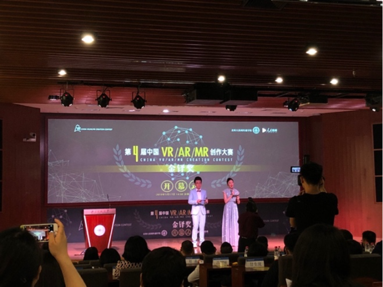 A man and a woman in formal wear, standing on a stage in front of a crowd.