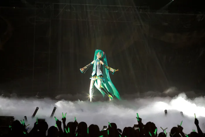 3D avatar with long green hair on a stage, in front of a crowd of people.